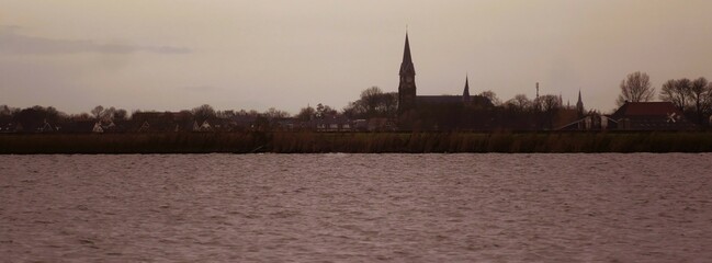 View of the village skyline from Oudega in Frisia Netherlands at dusk with the village church, in the foreground  the lake Aldegeaster Brekken,