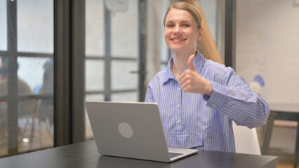 Thumbs Up by Young Woman Looking at Camera at Workspace