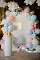 Charming first birthday party setup featuring a decorative arch adorned with a mix of pink, blue,...