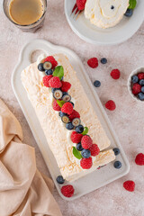 Meringue Pavlova roll cake with cream and fresh berries on top on a ceramic board on a concrete background. Copy space.