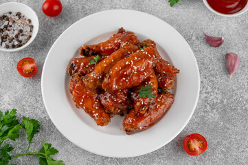 Baked chicken wings in a sweet chili sauce and sesame seeds on a white plate on a concrete...