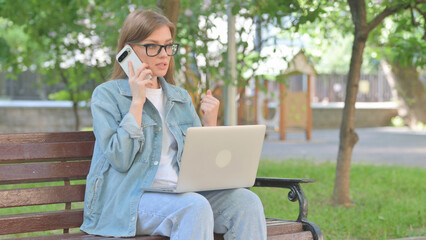 Young Woman Talking on Phone While Using Laptop