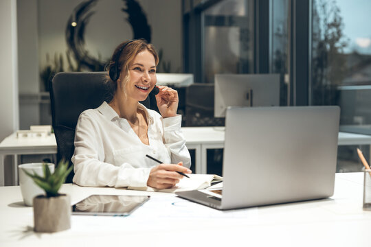 Female professional working on laptop with headset in modern office