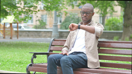 Obraz premium Waiting Young African Man Checking Wrist Watch on Park Bench