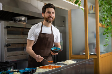 Man adds toppings pizza in kitchen working diligently preparing food