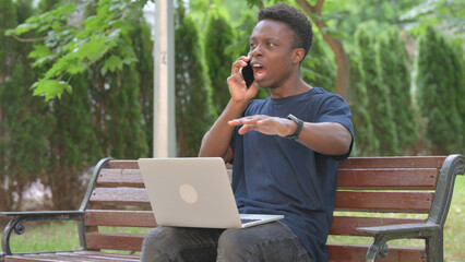 Angry African Man Talking on Phone While Using Laptop in Park