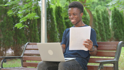 Casual African Man Reviewing Documents with Laptop in Park