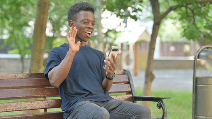 African American Man Doing Video Chat on a Phone, Sitting Outdoor