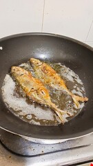 two marinated fish being fry in black frying pan. portrait format.