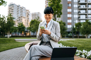 Business professional enjoys tech break in urban park while checking mobile phone