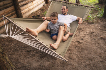 Father and son 5 years old fooling around playing relaxing in a hammock outdoors in a pine forest...