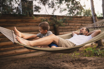 Father and son 5 years old fooling around playing relaxing in a hammock outdoors in a pine forest...