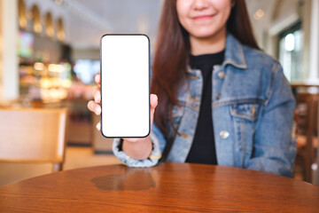 Mockup image of a woman holding and showing mobile phone with blank white screen in cafe