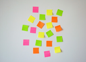 Obraz premium Random placed sticky notes in pink, yellow, green, and orange scattered on a white wall, symbolizing planning, brainstorming, reminders, and productivity. Ideal for office, education, creative work.