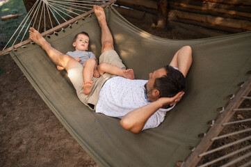 Father and son 5 years old fooling around playing relaxing in a hammock outdoors in a pine forest...