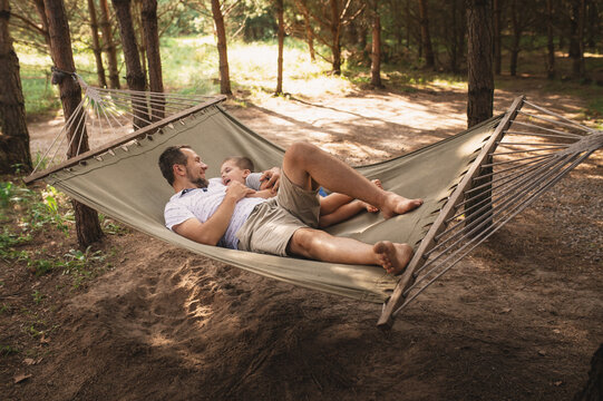 Father and son 5 years old fooling around playing relaxing in a hammock outdoors in a pine forest at a campsite. Tourism, active recreation, time spent with children - Powered by Adobe