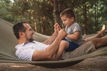 Father and son 5 years old fooling around playing relaxing in a hammock outdoors in a pine forest...