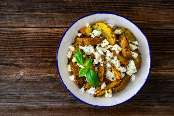Greek style roasted potatoes with feta cheese on wooden table