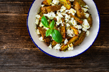 Greek style roasted potatoes with feta cheese on wooden table