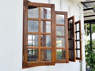 The view of the outer corner of the clean white-walled building shows dark brown wooden windows wide open, as well as vines decorating the walls, creating a warm and natural atmosphere.