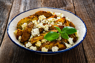 Greek style roasted potatoes with feta cheese on wooden table