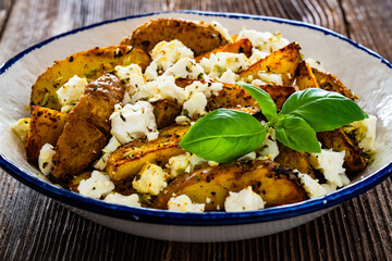 Greek style roasted potatoes with feta cheese on wooden table