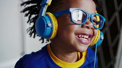 Young boy wearing blue and yellow shirt, headphones, and glasses experiencing musical joy with infectious smile, radiating pure childhood happiness while listening to favorite audio track - Powered by Adobe