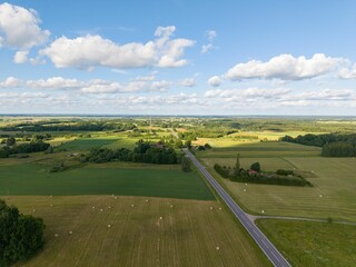 Aerial view of a rural landscape with fields, a road, and scattered clouds under a blue sky