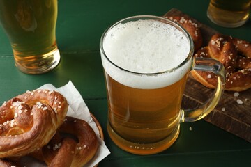 Tasty pretzels and glasses of beer on green wooden table, closeup