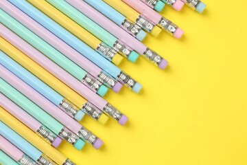 Many graphite pencils with erasers on yellow background, flat lay. Space for text