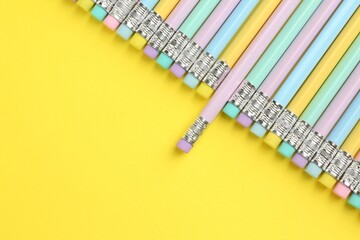Many graphite pencils with erasers on yellow background, flat lay. Space for text