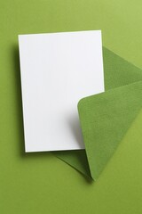 Blank invitation card and envelope on green background, top view. Space for design