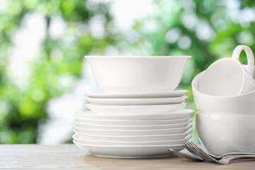 Different clean dishes on wooden table against blurred green background