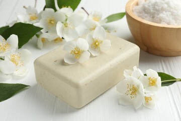 Soap bar, sea salt and jasmine flowers on white wooden table, closeup