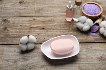 Soap bar, cosmetic products and cotton flowers on wooden table, above view