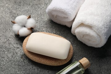 Soap bar, cosmetic product, cotton flower and towels on grey table, above view