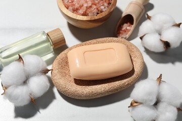 Soap bar, cosmetic products and cotton flowers on white marble table, above view