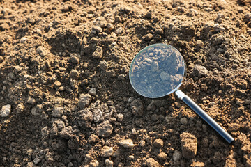 Magnifying glass on dry soil in field, above view. Space for text
