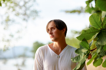 Contemplative Man in Nature Beneath Sunlit Leaves and Tranquil Background