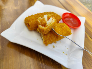 Crispy golden rissoles with savory and delicious filling, served on an elegant white plate, accompanied by a small bowl filled with bright red chili sauce and a fork, on the menu at an outdoor cafe.