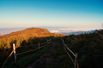 A scenic mountain path with wooden fences on either side, leading to a distant hill under a clear...