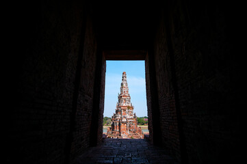 A view of an ancient temple spire framed by a dark brick corridor, with bright sunlight...