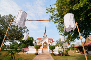 A traditional Thai temple with a red roof and white walls, surrounded by trees and decorated with...