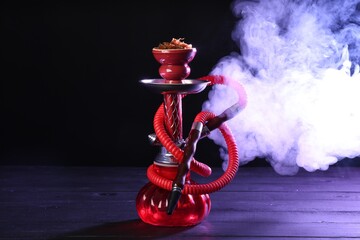 Hookah on wooden table with smoke in color lights against black background