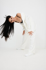 smiling woman in white suit bending forward with long black hair, casual and playful pose, studio...