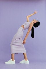 woman posing in lilac outfit stretches backward gracefully against soft purple studio background,...