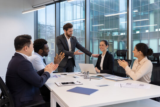 A diverse team celebrates a colleague's success in a modern office setting. Colleagues applaud and congratulate each other.
