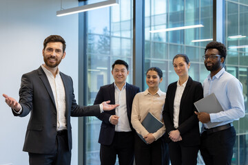 A diverse business team stands together in a modern office setting, ready to collaborate. They are...