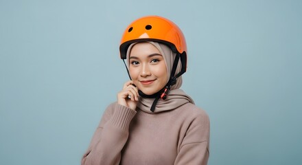 Young Woman Wearing Orange Safety Helmet and Casual Clothing Standing Against Light Blue Background