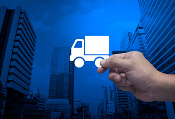 Hand holding delivery truck flat icon in fingers over modern office city tower and skyscraper, Business transportation service concept